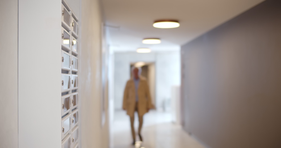 Senior man opening mailbox in lobby of apartment building and smiling receiving letter. Portrait of mature elegant grandfather receiving letter from grandchildren
