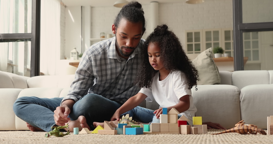 Caring young affectionate loving african american father playing toys with little cute biracial child daughter, sitting together on floor in modern living room, talking chatting communicating at home. Royalty-Free Stock Footage #1071379657