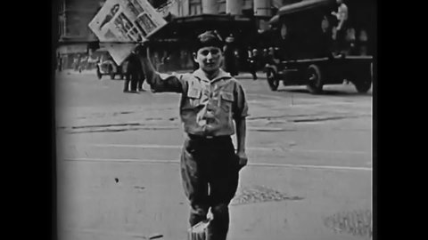 CIRCA 1928 - A newsie sells newspapers to passing pedestrians on a city street.