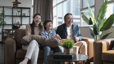 Happy Asian family spending time by watching tv together on sofa in living room. family and home concept