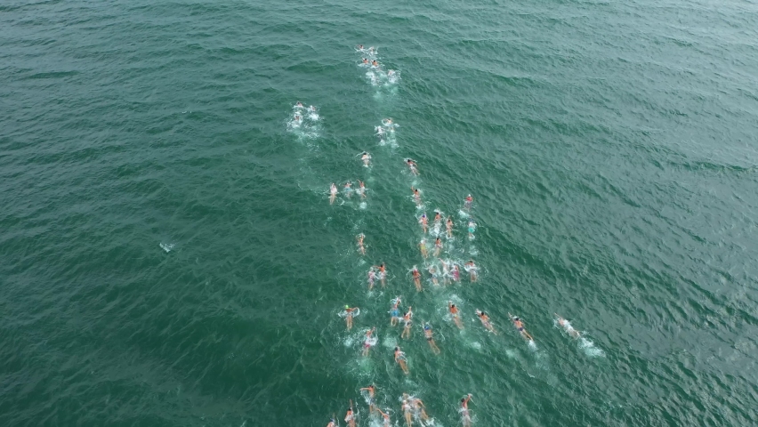 Aerial Drone Shot 4K of Triathlon Swimming Race. Ironman Competition. Traditional swimming marathon in Varna, Bulgaria. A huge group of people invades the water. Start swimming in the sea or ocean. Royalty-Free Stock Footage #1071389914