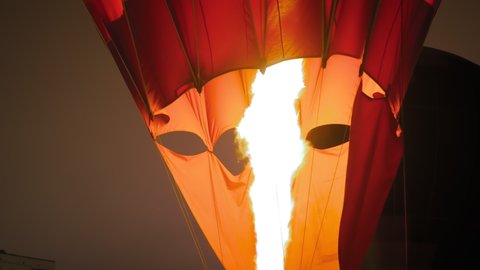 Fire from gas jet burner inflating hot air balloon during outdoor aerostat festival at night - flame rising in dark