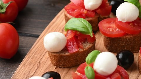 Cooking italian food bruschetta with tomatoes, black olives, mozzarella and basil. bruschetta is poured with balsamic glaze. typical Italian antipasti starter in restaurant in Italy Rome Milan. 