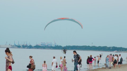 Sopot, Poland 01.08.2020 - Paraglider taking off over the beach. Bunch of people on the shore enjoying. Beautiful clear blue sky in the background. Man under the canopy of the parachute can be seen