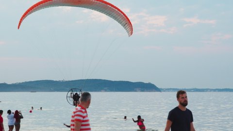 Sopot, Poland 01.08.2020 - Man under the orange little canopy of a parachute taking off over the beach. Scenic cloudy blue sky in the background. People can be seen enjoying themselves on the beach. 