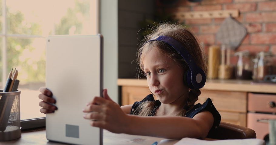 Cute small  kid girl in headphones using funny editing application on digital computer tablet, enjoying cool video or photo content in social network, playing online games, communicating distantly. | Shutterstock HD Video #1071403318