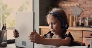 Cute small  kid girl in headphones using funny editing application on digital computer tablet, enjoying cool video or photo content in social network, playing online games, communicating distantly.