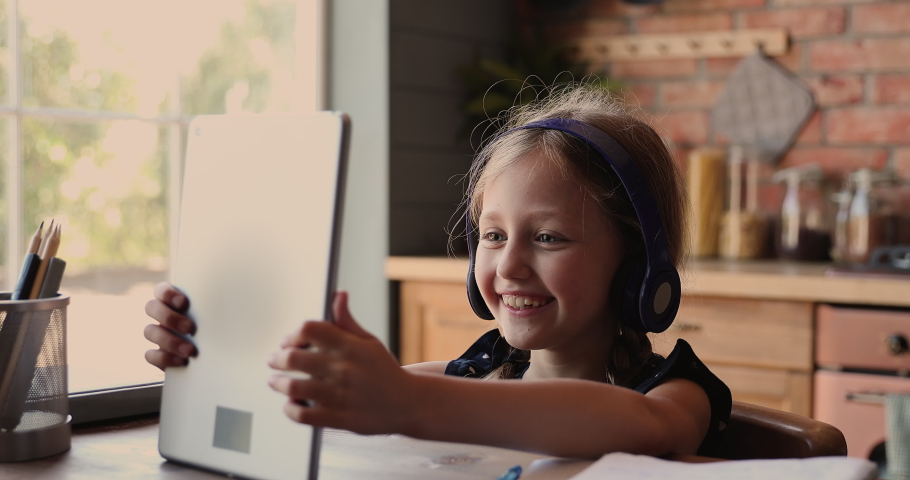 Cute small  kid girl in headphones using funny editing application on digital computer tablet, enjoying cool video or photo content in social network, playing online games, communicating distantly. Royalty-Free Stock Footage #1071403318