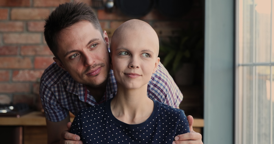 Affectionate young man cuddling shoulders of smiling hairless 25s woman, supporting beloved wife during oncology cancer disease treatment, feeling hopeful looking at camera, struggle for life concept. Royalty-Free Stock Footage #1071403381