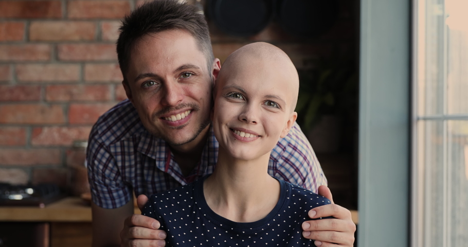 Affectionate young man cuddling shoulders of smiling hairless 25s woman, supporting beloved wife during oncology cancer disease treatment, feeling hopeful looking at camera, struggle for life concept. Royalty-Free Stock Footage #1071403381