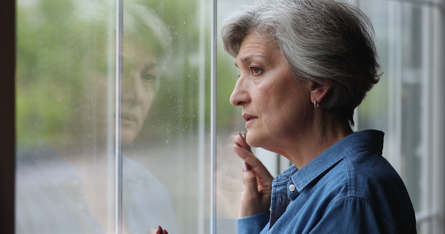 Head shot frustrated unhappy unhealthy middle aged retired woman looking out of window, suffering from negative melancholic thoughts or feeling lonely alone indoors, ageing process concept. Royalty-Free Stock Footage #1071403396