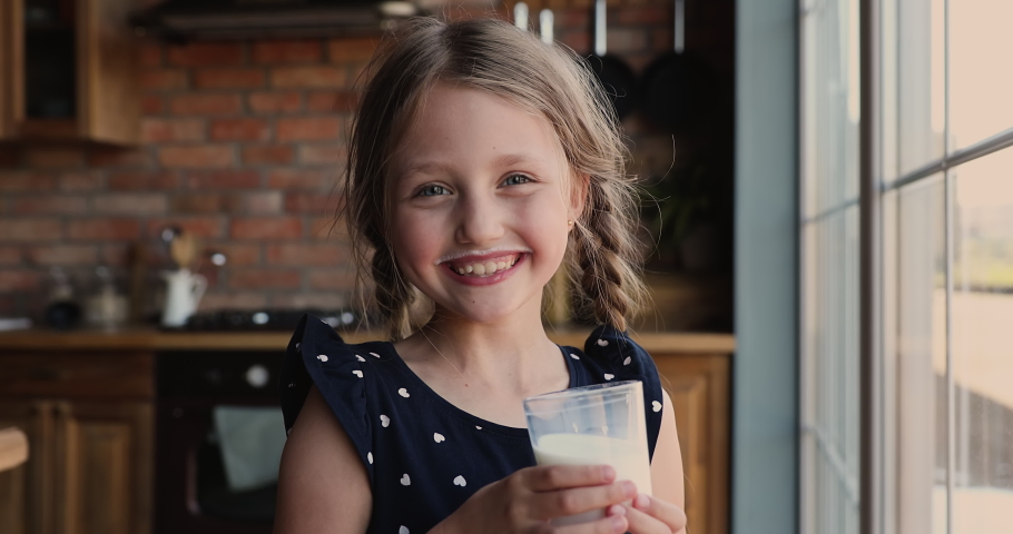 Head shot funny cute little 7s kid girl drinking glass of sweet organic yoghurt in morning looking at camera showing milk mustache, enjoying healthy beverage, children healthcare lifestyle concept. | Shutterstock HD Video #1071403477