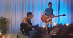 Father and son play guitar at home. Dad teaches child to play musical instruments. Music hobby, Create, learning own songs. SHARE THE LOVE, play our game. 4K video.

