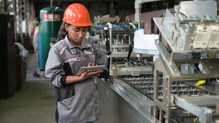 A young black manufacturing worker controls an assembly line in a factory, making notes on a tablet. Young woman in hard hat watches the work process | Shutterstock HD Video #1071410221