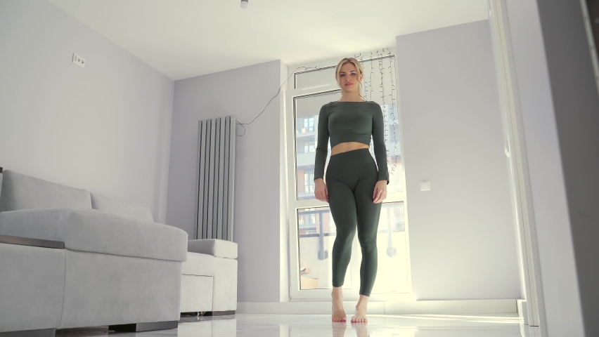 young athletic fit woman performs aerobics and gymnastics exercises at home. Fitness sporty Female in sportswear does stretching legs and arms in living room. Workout warm-up before training indoors