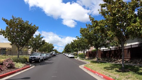 4K HD video driving point of view through new housing in a generic housing neighborhood, school on the left houses on the right. Blue cloudy skies in the backgrounds.