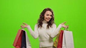 The woman is looking at the camera and smiling. She is raising up the shopping bags. She's very happy. She is standing on a green background. Green screen. 4K - Powered by Shutterstock - Get 15% off with code: PIKWIZARD15