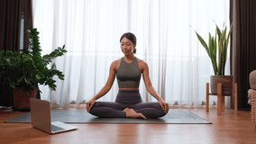 Asian woman practicing yoga from yoga online course on a video conference on a laptop at home. Healthy lifestyle - technology at home. New normal lifestyle