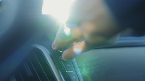 Car radio. The hand turns the volume of the radio in the car. Close up of radio volume. Car interior in the rays of the sun. Music in the car. Modern music technology. Man's hand on volume button