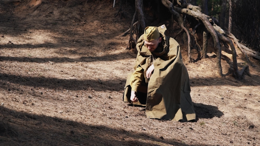 A Red army soldier with a cap on his head touches the ground with his hand, which crumbles down. Slow motion images