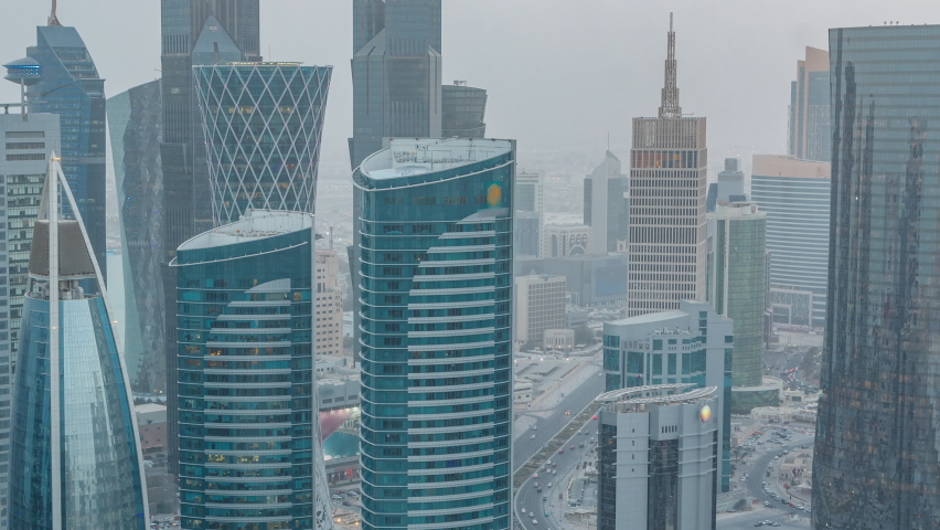 Skyline of the West Bay area from top in Doha day to night transition timelapse, Qatar. Illuminated modern skyscrapers aerial view from rooftop at evening after sunset. Traffic on the road