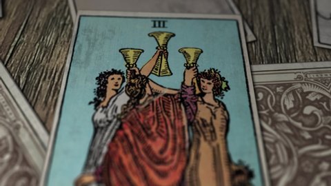 Bratislava, Slovakia - January 10, 2021. The Three Of Cups shows Multiple Young Females wearing long different colored robes and raising their cups high in the air. Tarot Card. Cartomancy. Divination.