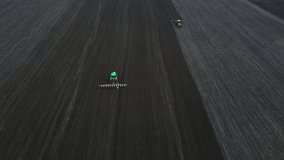 Aerial view of a two modern green tractors plowing dry agricultural field and seeding , preparing land for sowing, spring, drone video.