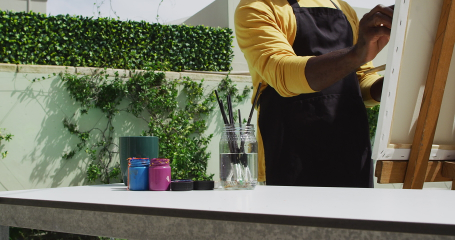 African american senior man standing on a terrace and painting. retirement hobby and outdoor leisure time.