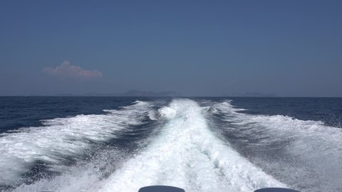 Waves from the engines of a high-speed boat. Rear view. Blue sky, white cloud and far island. White foam from waves. Floating in the ocean.