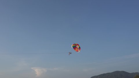 A man and an instructor are flying on a parachute. Active holidays on the beach in summer. The landing parachutist. The parachute is tied to the boat. Extreme rest. Phuket, Thailand.