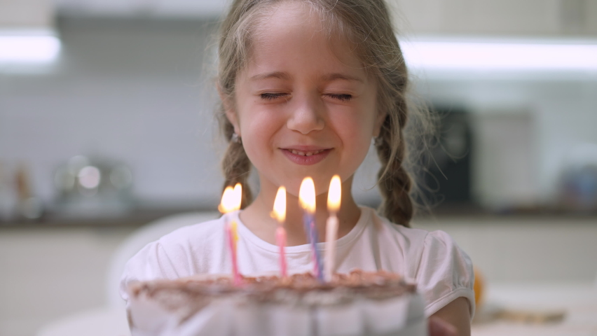 Close-up of charming little girl with closed eyes making wish and blowing candles on birthday cake. Portrait of happy Caucasian pretty child celebrating birthday indoors at home. Joy and lifestyle | Shutterstock HD Video #1071429889