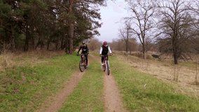 Slow motion aerial shot of young sport men ride bicycles on forest road at spring cloudy evening. Healthy cycling lifestyle, 4k footage