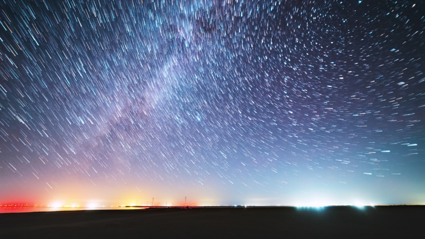 Magic night landscape with moving star trails and Milkyway Galaxy and flashing light from wind turbines farm reflected from lake. Starry night landscape with moving star trails in night sky. | Shutterstock HD Video #1071434161
