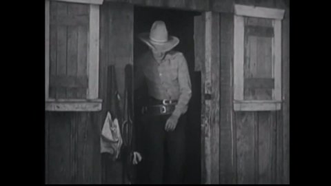 CIRCA 1934 - In this western film, a cowboy (John Wayne) hides from bandits and uses a lasso to tie them up outside a barn.