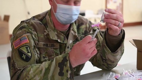 CIRCA 2021 - U.S. Army medical soldiers draw from vials for innoculating and injecting people COVID-19 pandemic vaccines.