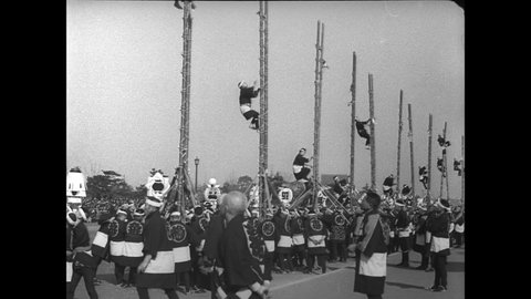 CIRCA 1932 - Firemen stage a processional and perform stunts while climbing bamboo ladders in Tokyo, Japan.