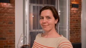 Cheerful young woman with a glass of red wine congratulating and toasting while having a videocall. Social distancing and isolation concept, communication at quarantine, coronavirus pandemic