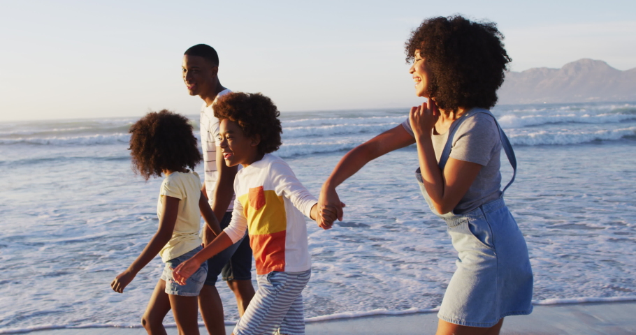 African american mother and son dancing together during sunset at the beach. family travel vacation leisure concept