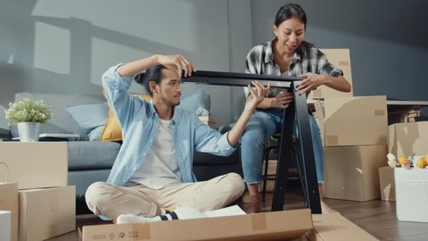 Happy asia young attractive couple man and woman help each other unpacking box and assemble furniture decorate house build table with carton box in living room. Young married asian move home concept.