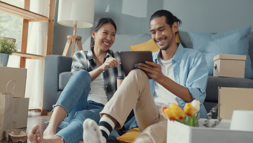Happy asian young attractive couple man and woman use tablet online shopping furniture decorate house with carton package move in new house. Young married asian moving home shopper online concept. | Shutterstock HD Video #1071449545