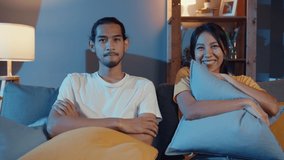 Romantic asia couple man and woman smile and laugh lay down on sofa in living room at night watch comedy movie on television together at home. Married couple family lifestyle, stay at home concept.