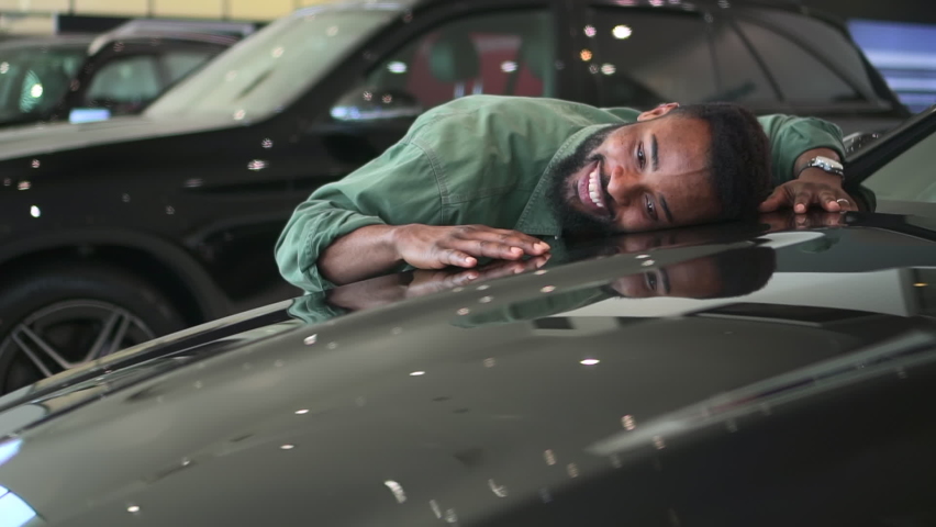 Buy car, happy funny man hugging stroking auto hood that he purchased in dealership. 
