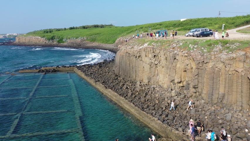 Aerial view of a marine ranch (fish farming) enclosed by jetties at the beautiful coast and tourists enjoying a panoramic view atop the columnar basalt on a sunny summer day, in Xiyu, Penghu, Taiwan Royalty-Free Stock Footage #1071451108