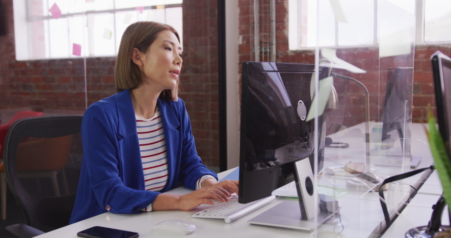Asian businesswoman sitting at desk using computer and passing document over sneeze guard. working in a modern office Royalty-Free Stock Footage #1071451198
