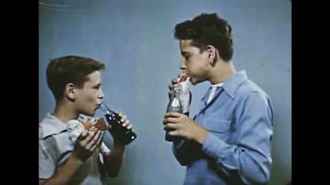 CIRCA 1950 - Two boys eat hamburgers and drink Coke.