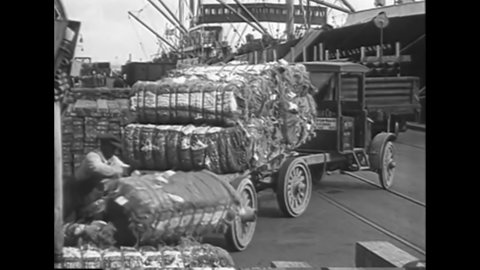 CIRCA 1919 - Bales of cotton are unloaded from trucks onto a dock in the south.