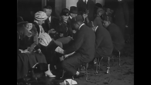 CIRCA 1920 - African-American employees lace up white women's skates at an indoor ice rink and couples skate together.