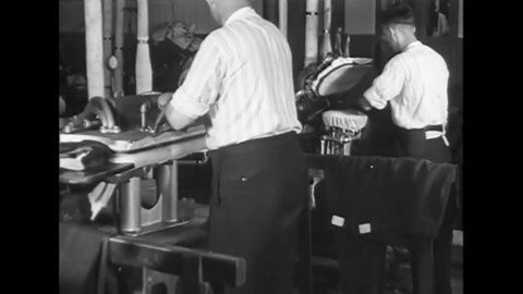 CIRCA 1920 - Women use sewing machines and men press the clothes in a clothing factory.