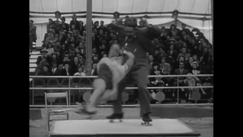 CIRCA 1950s - A roller-skating couple performs a stunt at a circus where the man twirls his partner around on a rope held by his teeth.