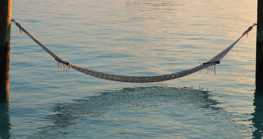 Hammock over ocean waves on bright sunny day. Perfect for travel, tourism, vacation, honeymoon holiday background graphics. Hammock reflection on water and relaxing scenic ocean landscape